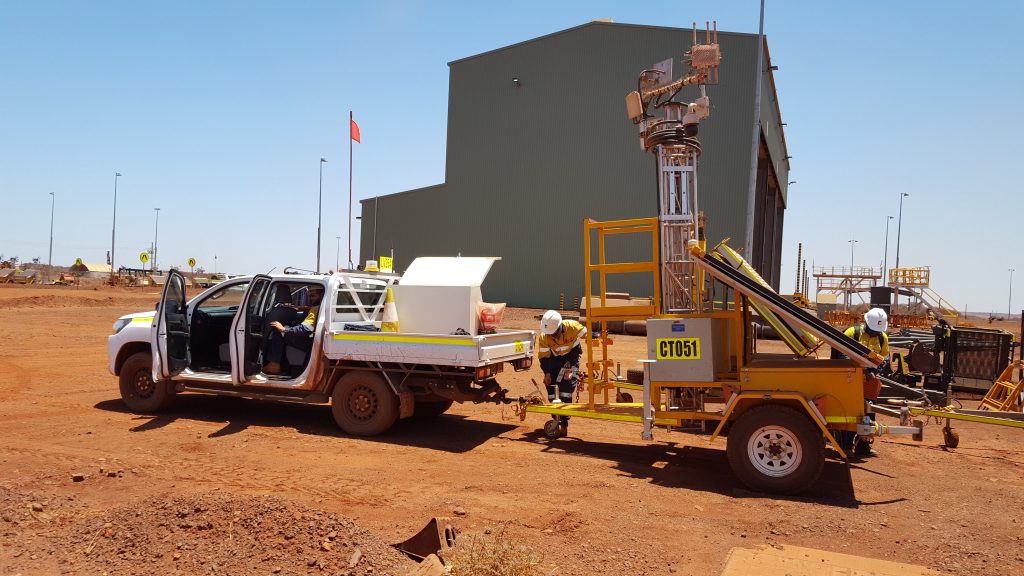 An orange Aluma aluminum telescoping tower trailer system on wheels attached to a white truck