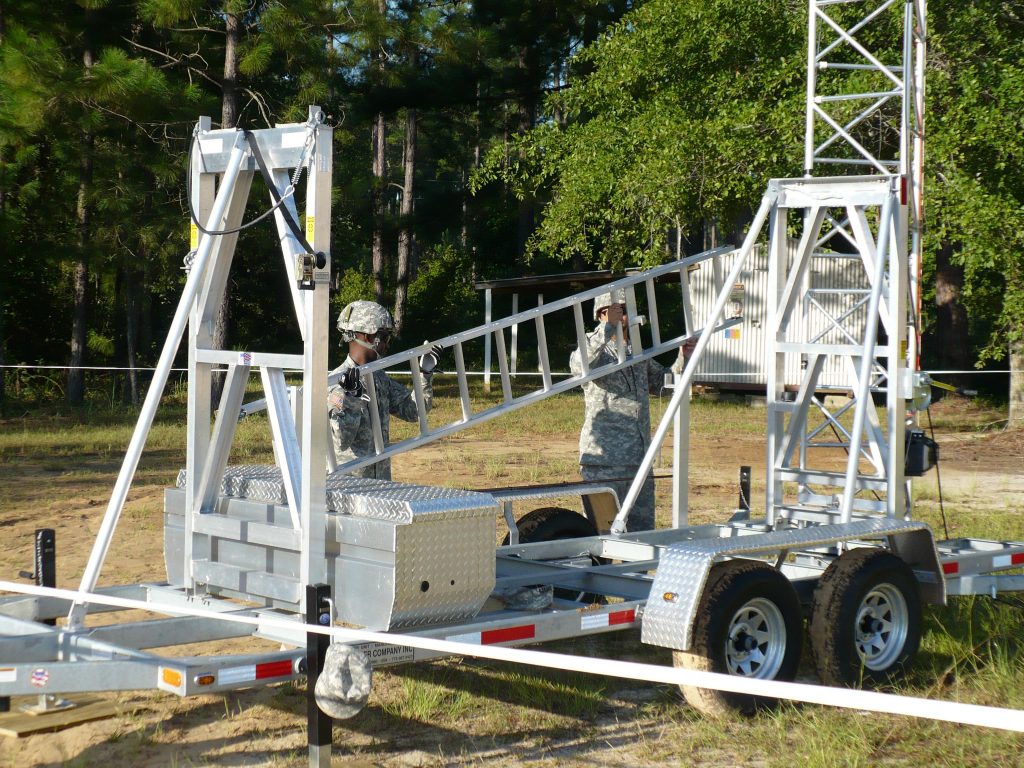 Two people attaching a ladder to an Aluma aluminum telescoping tower-trailer system on wheels
